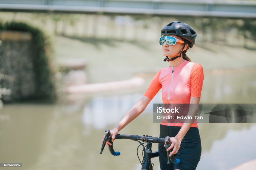 Portrait asian chinese female cyclist standing with road bike during weekend morning at rural scene looking away with cool attitude 20-24 Years Stock Photo
