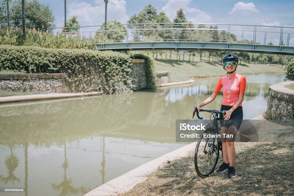 Portrait asian chinese female cyclist standing with road bike during weekend morning at rural scene looking at camera smiling 20-24 Years Stock Photo