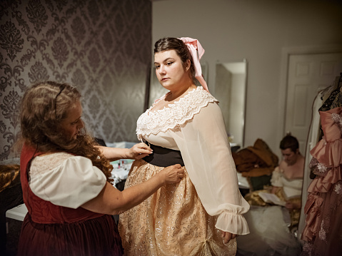 Three Actresses in period costumes in dressing room. Getting ready for stage performance. Last minute adjusting of make up, and hair. Interior of dressing room  of Theatre building at night.