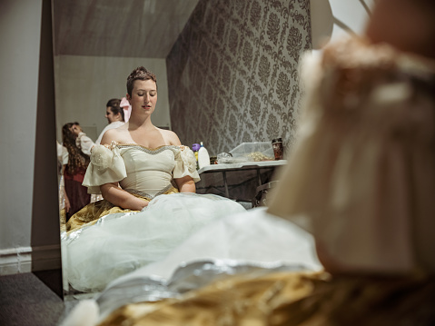 Three Actresses in period costumes in dressing room. Getting ready for stage performance. Last minute adjusting of make up, and hair. Interior of dressing room  of Theatre building at night.