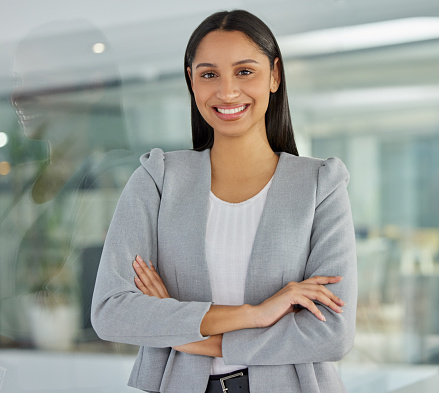 Business woman in her 40's looks away thoughtfully in an office. Professional woman standing in a suit with crossed arms.