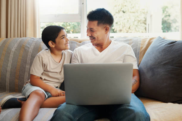 istock Shot of a handsome young man sitting on the sofa and bonding with his son while using a laptop 1349321701