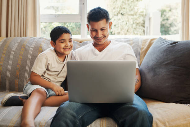 istock Shot of a handsome young man sitting on the sofa and bonding with his son while using a laptop 1349321703