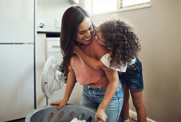집에서 세탁물로 그녀를 돕는 동안 그녀의 어머니를 껴안고 사랑스러운 어린 소녀의 샷 - washing 뉴스 사진 이미지
