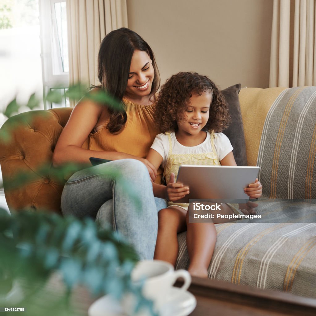 Shot of an attractive young woman and her daughter sitting on the sofa at home and using technology She can watch as many educational shows as she likes Family Stock Photo