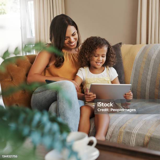 Shot Of An Attractive Young Woman And Her Daughter Sitting On The Sofa At Home And Using Technology Stock Photo - Download Image Now