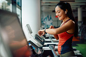 istock Happy Asia athletic woman using fitness tracker while running on treadmill in a gym. 1349328573