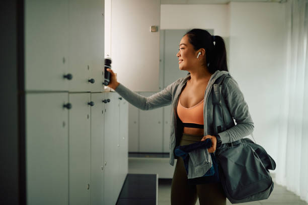 Happy Asian female athlete preparing for workout at gym's locker room. Happy Asian athletic woman taking her stuff from a locker after finishing sports training in a gym. locker room stock pictures, royalty-free photos & images
