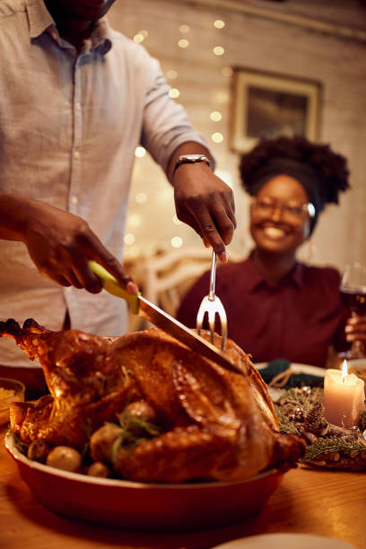 zbliżenie czarnego mężczyzny rzeźbiącego indyka na święto dziękczynienia przy stole jadalnym. - roast turkey turkey cutting roasted zdjęcia i obrazy z banku zdjęć