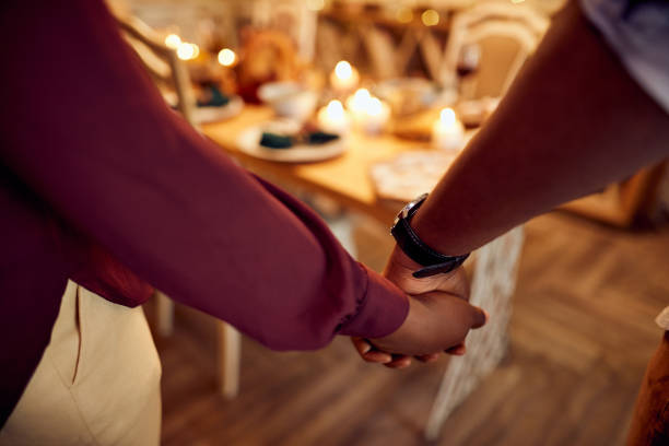 Close-up of African American couple holding hands at dining room while celebrating Thanksgiving at home. Close-up of black couple saying grace while holding hands during Thanksgiving meal in dining room. saying grace stock pictures, royalty-free photos & images