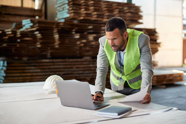 istock Warehouse manager using laptop while going thorough distribution plans at lumber department. 1349328730