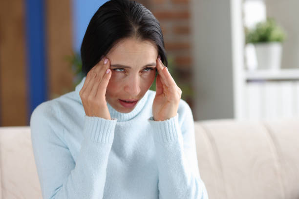 istock Woman with headache holds hands at temples while sitting on couch 1349329674