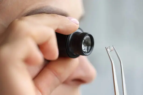 Woman looks through magnifying glass at precious stone. Stone authentication concept