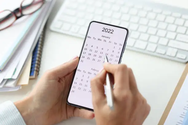 Smartphone on screen with calendar for 2022 pen in female hands. Planning business ideas for 2022 concept