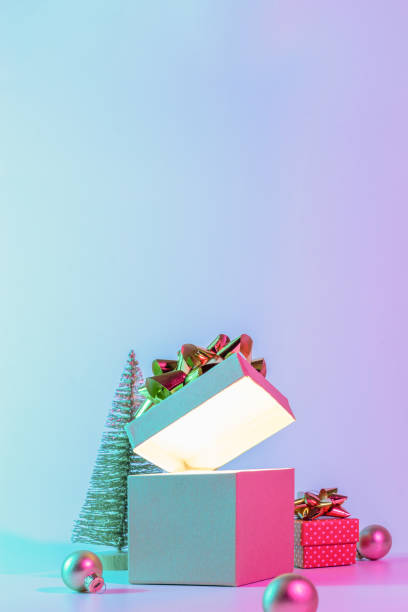istock Neon Christmas winter background. Open xmas gift box with shine lights, minimal tree. Holiday decoration bauble ball on neon abstract gradient backdrop. Happy new year copy space. 1349333861