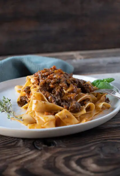 Italian cuisine dish with a delicious duck ragout alla bolognese served with tagliatelle isolated on a plate on wooden background.