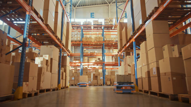 istock Future Technology 3D Concept: Automated Modern Retail Warehouse AGV Robots Transporting Cardboard Boxes in Distribution Logistics Center. Automated Guided Vehicles Delivering Goods, Products, Packages 1349338190
