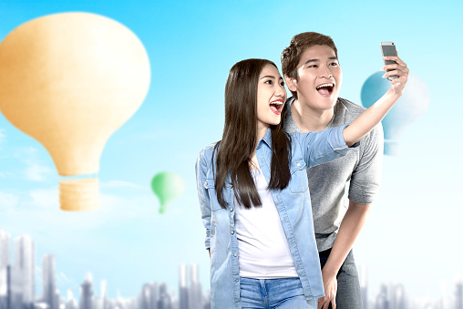 Asian couple taking a selfie with colorful air balloon flying with cityscape background