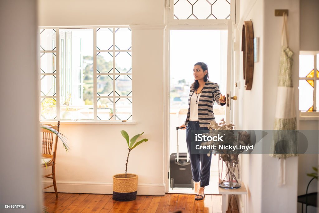 Young woman with a suitcase arriving at her vacation rental accommodation Young woman pulling a suitcase opening the front door of her rental accommodation during a vacation trip Vacation Rental Stock Photo