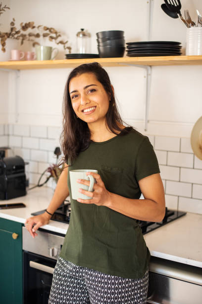 istock Smiling young woman in pajamas drinking coffee in her kitchen 1349342924