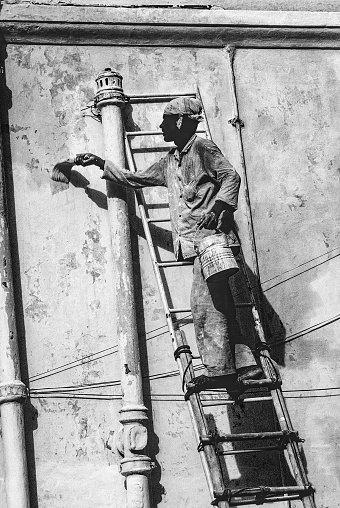 Jaisalmer, India - June 30, 1994: local painter paints the old wall in Jaisalmer, India. The ladder is self made by wooden sticks.