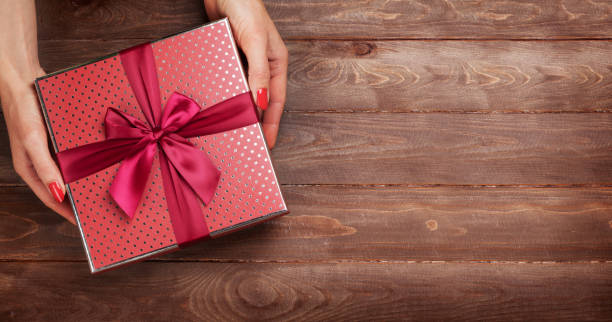 istock Female hands holding gift above wooden table 1349346376
