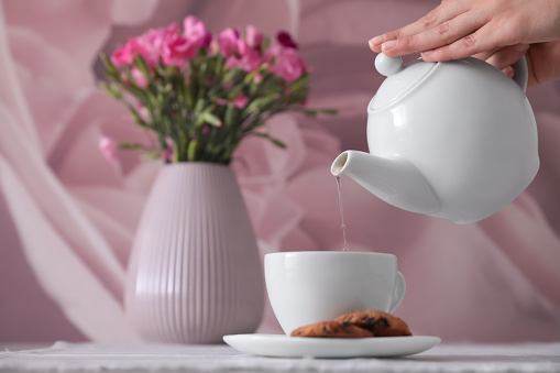 Woman pouring hot tea into cup at table, closeup