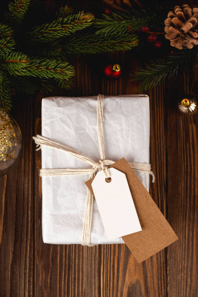 istock Christmas Gift Tag mockup. White minimal gift box on wooden table with festive decorations. 1349352963