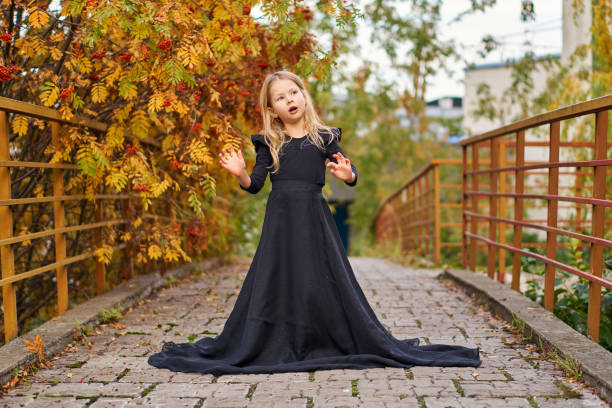 feliz garotinha rindo em uma trilha de outono em um longo vestido preto moda. halloween em um lindo vestido de princesa. terno retrô e sorriso. rindo menina criança engraçada em uma fantasia de bruxa no halloween - little girls autumn child red hair - fotografias e filmes do acervo