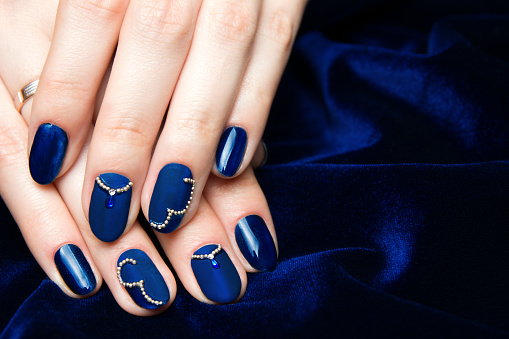 French manicure - beautiful manicured female hands with classic blue manicure with rhinestones on dark blue background