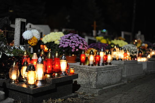 Candle lights on graves and tombstones in cemetery at night in Poland on All Saints’ Day or All Souls’ Day or Halloween or Zaduszki or Day of the Dead in Europe