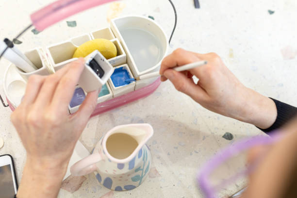 istock Women's hands mix paint for coloring ceramic milk jug in workshop 1349366143