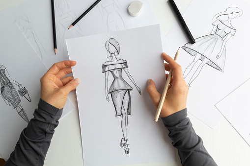 The designer draws sketches of women's dresses on paper.