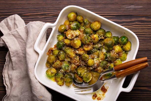 Vegetarian roasted brussels sprouts on wooden table Healthy vegetarian dish roasted brussels sprouts with butter and parmesan cheese in white ceramic casserole top view on dark rustic wooden table from above, vegan food brussels sprout stock pictures, royalty-free photos & images