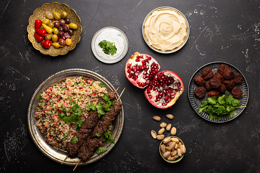 Various Turkish dishes: meat kebab with tabbouleh salad, falafel, hummus, olives, pistachios and Middle Eastern meze on black concrete table top view. Ethnic arab food, cuisine of Turkey