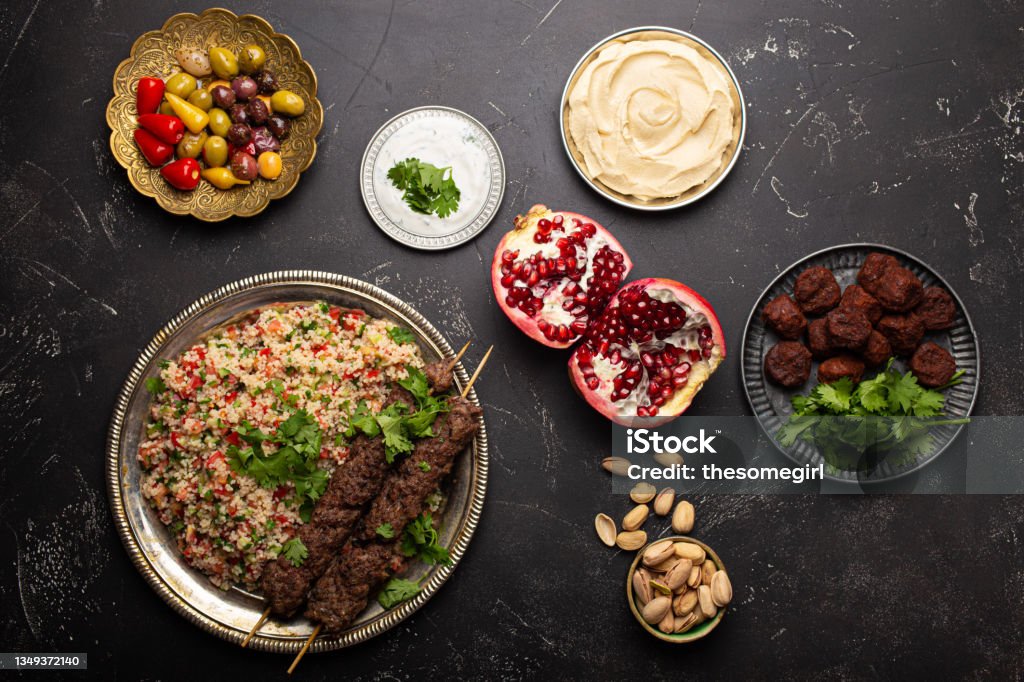 Arab Turkish assorted food from above Various Turkish dishes: meat kebab with tabbouleh salad, falafel, hummus, olives, pistachios and Middle Eastern meze on black concrete table top view. Ethnic arab food, cuisine of Turkey Meze Stock Photo