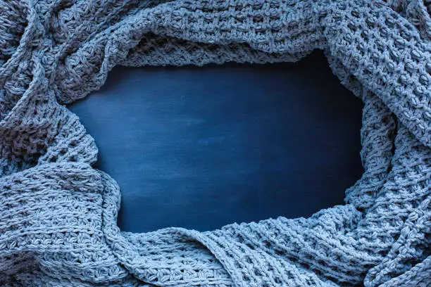 Photo of Grey woven blanket crumpled and framed over a blue toned black wooden background