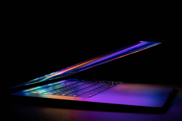 a laptop half closed bright and glowing a laptop half closed bright and glowing in a dark background. isolated on dark stock pictures, royalty-free photos & images