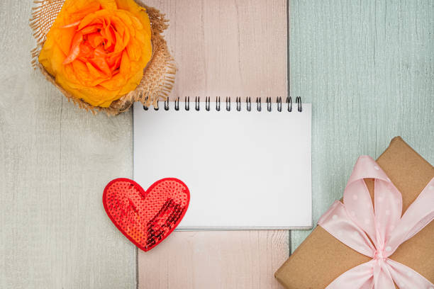 istock Rose, heart, notebook with a blank sheet and a gift on a colored wooden background. Flat lay 1349374883