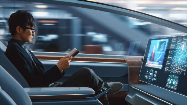 Futuristic Concept: Handsome Stylish Japanese Businessman in Glasses Reading Notebook and Watching News on Augmented Reality Screen while Sitting in a Autonomous Self-Driving Zero-Emissions Car. Futuristic Concept: Handsome Stylish Japanese Businessman in Glasses Reading Notebook and Watching News on Augmented Reality Screen while Sitting in a Autonomous Self-Driving Zero-Emissions Car. driverless transport stock pictures, royalty-free photos & images