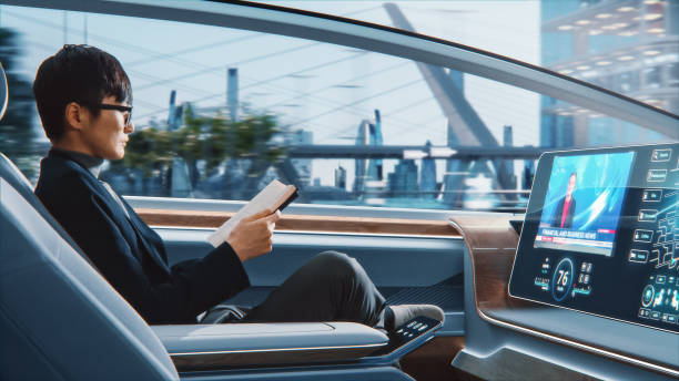 Futuristic Concept: Handsome Stylish Japanese Businessman in Glasses Reading Notebook and Watching News on Augmented Reality Screen while Sitting in a Autonomous Self-Driving Zero-Emissions Car. Futuristic Concept: Handsome Stylish Japanese Businessman in Glasses Reading Notebook and Watching News on Augmented Reality Screen while Sitting in a Autonomous Self-Driving Zero-Emissions Car. autopilot stock pictures, royalty-free photos & images