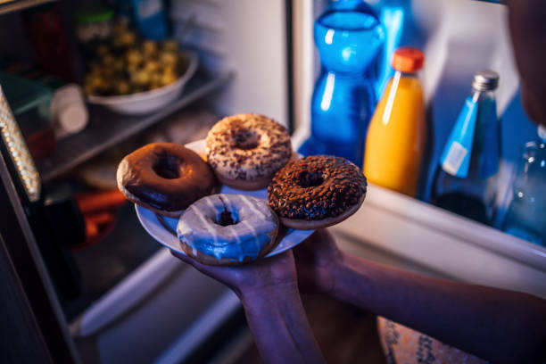 mujer sacando rosquillas de la nevera - comer demasiado fotografías e imágenes de stock