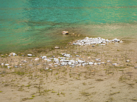 Reservoir during a drought, a rocky shoal. A pile of rocks on the muddy bottom. Turquoise water of a mountain river.