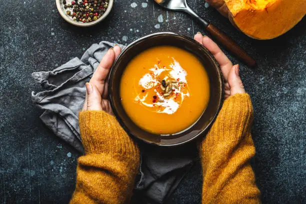 Photo of Female hands with bowl of pumpkin soup