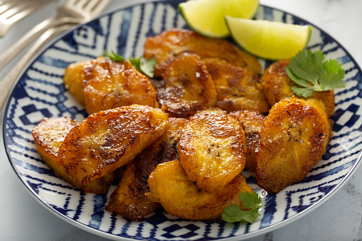 Fried caramelized plantains served with lime wedges and cilantro