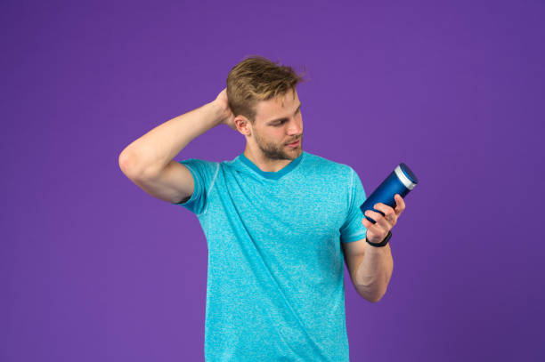 istock Man on confident face touching his hair, violet background. Guy with bristle holds bottle with shampoo, copy space. Man enjoy freshness after washing hair with shampoo. Hair care and shampoo concept 1349384036