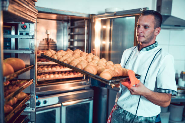 istock Male Baker Storing Freshly Baked Croissants On Baking Shelves 1349390949