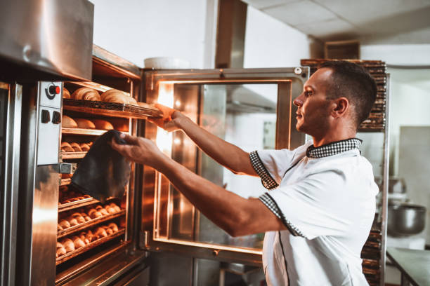 panettiere maschio che controlla le condizioni dei dolci freschi in forno - baking baker bakery bread foto e immagini stock