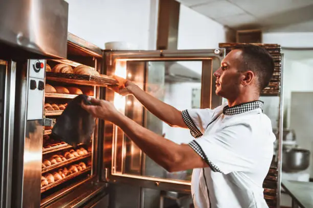 Male Baker Checking Condition Of Fresh Pastries In Oven