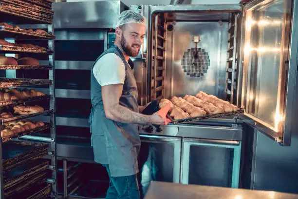 Smiling Bearded Baker Taking Out Croissants Before Burning In Oven
